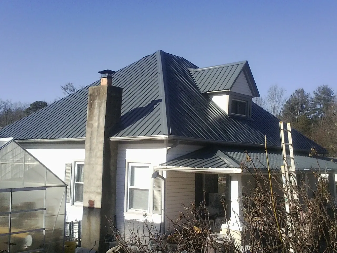 Dark blue standing seam metal roof on a white farmhouse with dormer — Slate & Tile Roof Repair by Roofing Brothers in Carriere