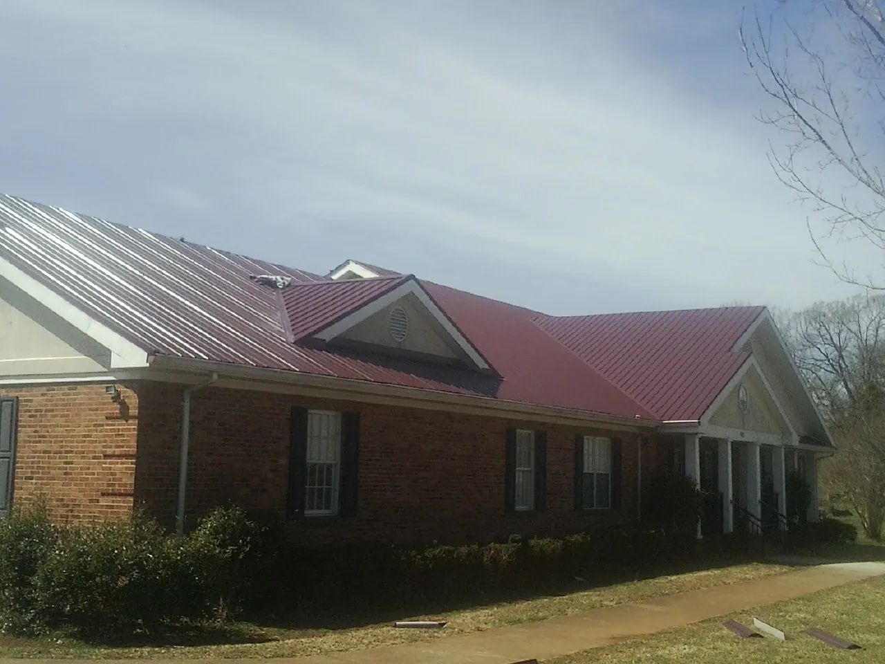 Red metal roof with gabled entries on a long brick building, from a Hail Damage Roof Repair job in Carriere