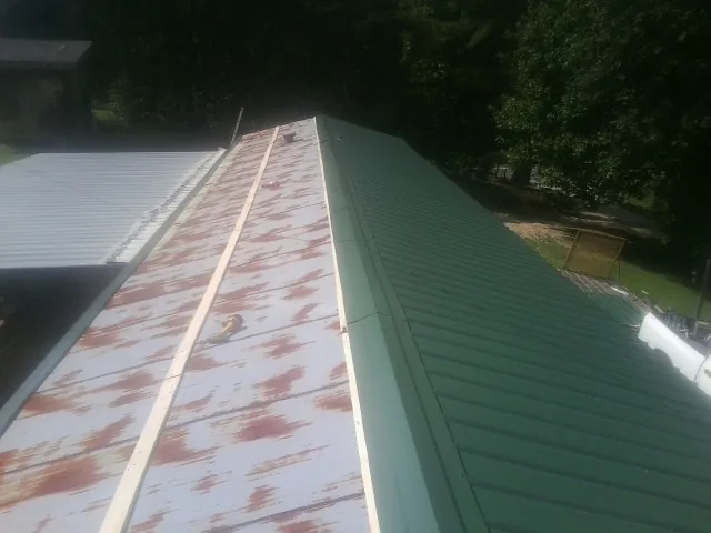 Old rusted panels beside newly installed green metal roofing — Wind Damage Roof Repair by Roofing Brothers in Carriere