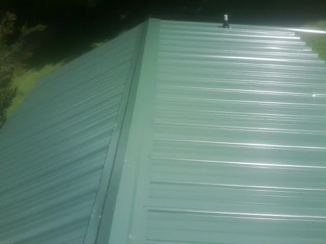 New green metal panels meeting at the ridge of a roof — Flat Roof Repair work by our crew in Carriere