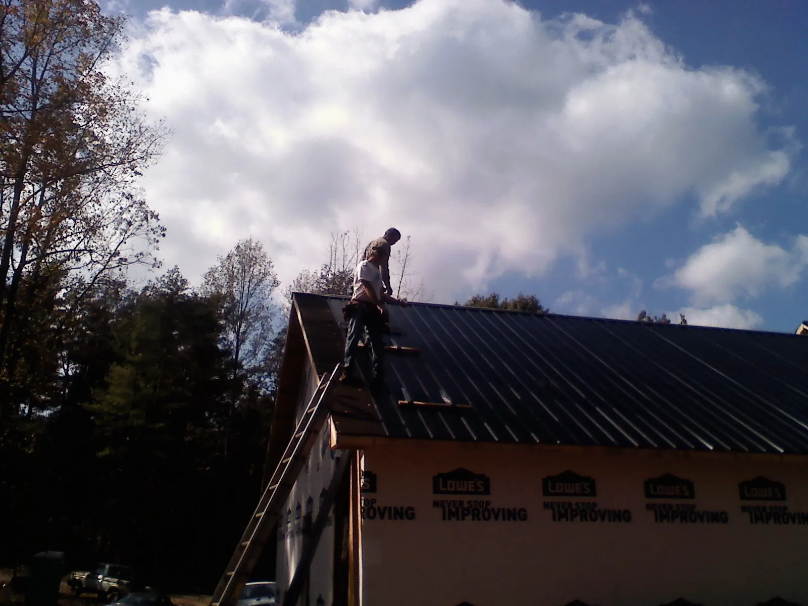 Roofer fastening dark metal panels high against a cloudy sky, from a Roof Inspection job in Carriere