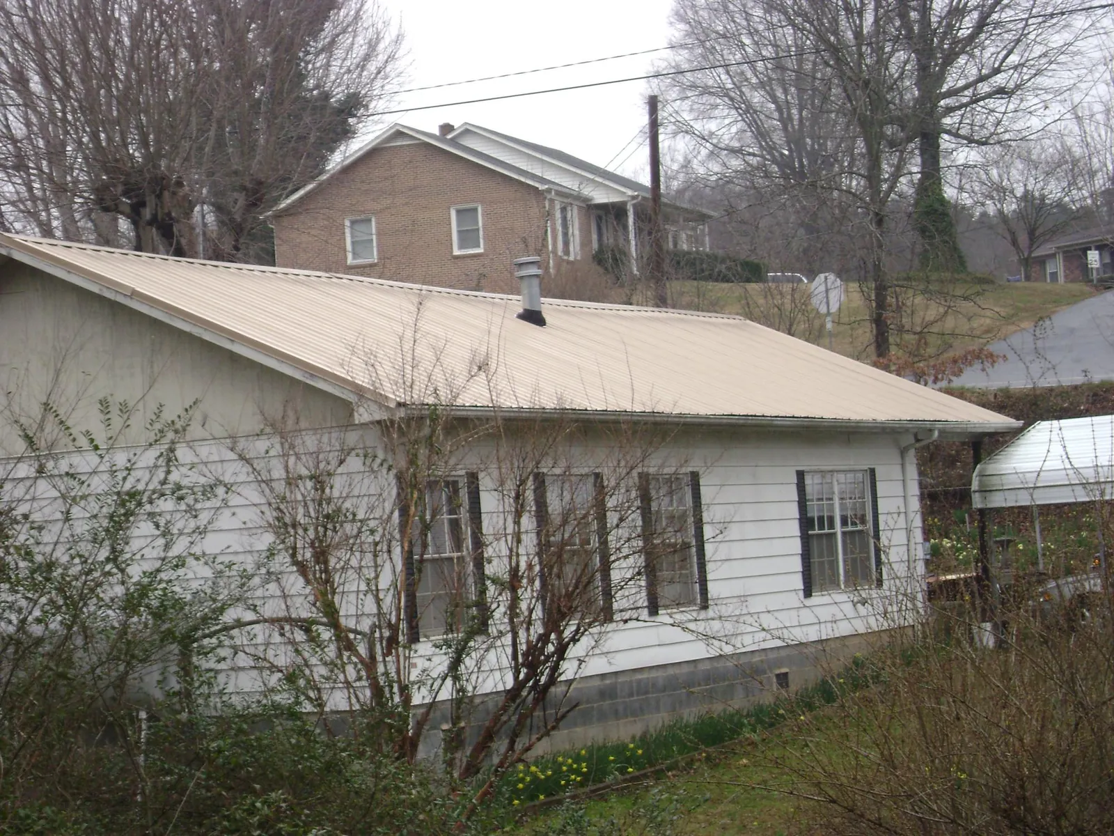Tan metal roof on a white sided house set into a hillside — Commercial Roofing by Roofing Brothers in Carriere