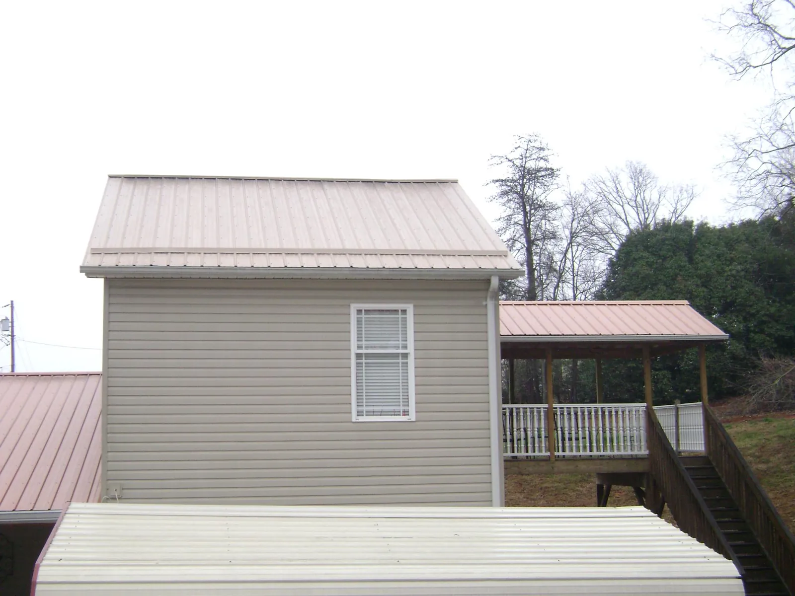 Tan metal roofs on a two story addition and attached porch, from a Roof Replacement job in Carriere